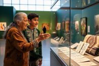 An Elder and a young visitor in a Saskatchewan museum share language-learning materials in a warmly lit gallery space.