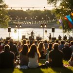 People gathered at an outdoor music stage during a warm summer evening festival near the South Saskatchewan River in Saskatoon.