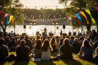 People gathered at an outdoor music stage during a warm summer evening festival near the South Saskatchewan River in Saskatoon.