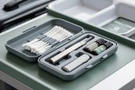 Open hard-shell Q-tip travel case with cotton swabs and separate compartments holding a vape pen and CBD oil vials, arranged neatly for travel.