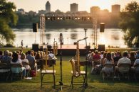Outdoor jazz festival stage on Saskatoon’s riverbank at sunset with brass instruments, microphones, and a small seated crowd.