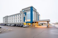 Exterior view of the Saskatoon Travelodge on Circle Drive West with driveway and parking area under a bright overcast sky.