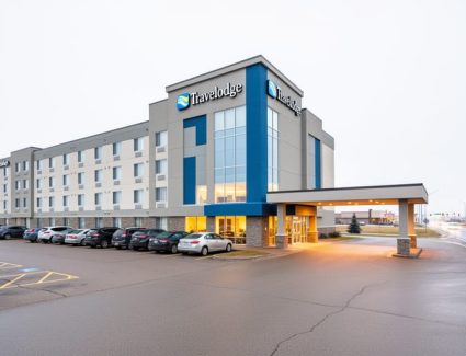 Exterior view of the Saskatoon Travelodge on Circle Drive West with driveway and parking area under a bright overcast sky.