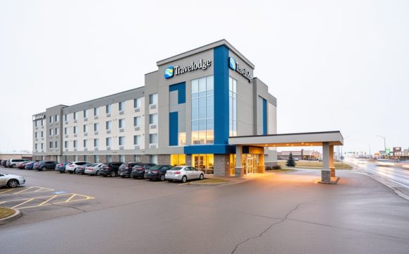 Exterior view of the Saskatoon Travelodge on Circle Drive West with driveway and parking area under a bright overcast sky.