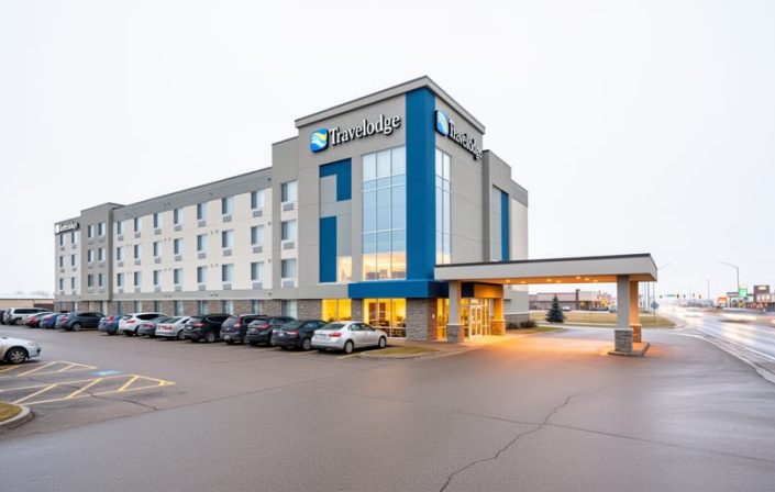 Exterior view of the Saskatoon Travelodge on Circle Drive West with driveway and parking area under a bright overcast sky.